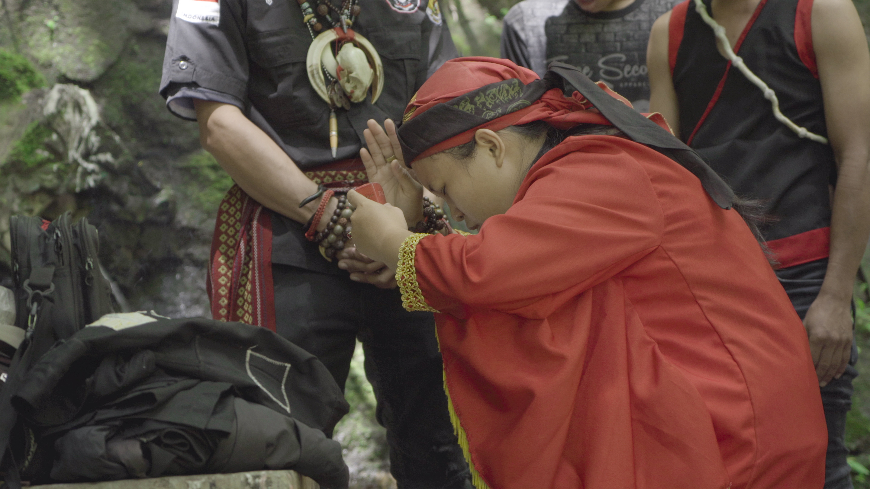 sjamaan bidt met gebogen rug, gekleed in een rood gewaad en hoofddeksel, omringd door toeschouwers